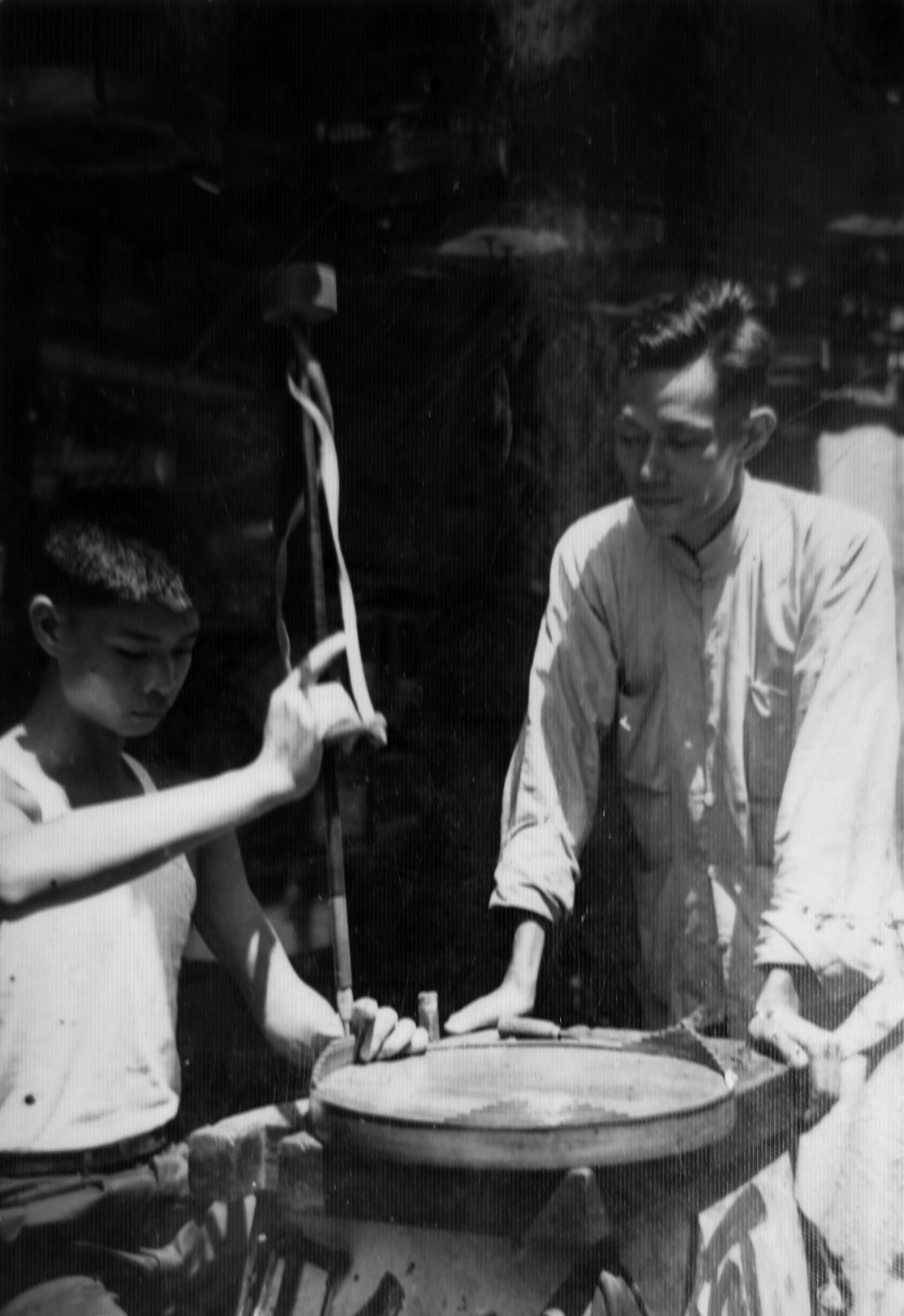 卓康師傅（右）正在指導手持鑽孔工具的徒弟陳樂財（左）製作鳥籠，約攝於1950年代末。圖片來源：陳樂財師傅提供。